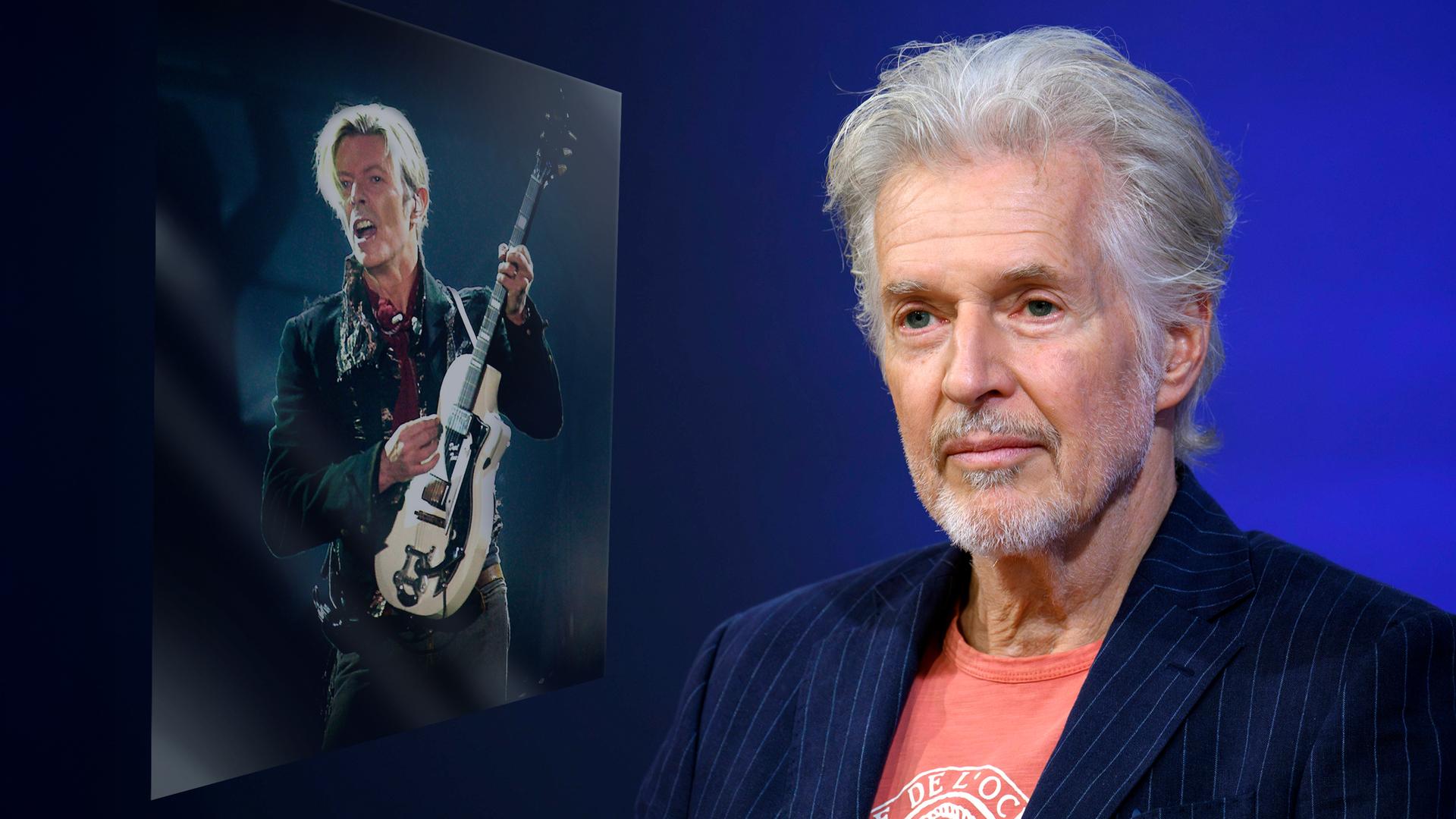 Ein älterer Mann mit grauem Haar und in T-Shirt und Jacket blickt mit einem dezenten Lächeln in die Kamera. Links von ihm ist ein Bild von einem Mann, der auf der Bühne E-Gitarre spielt, eingeblendet