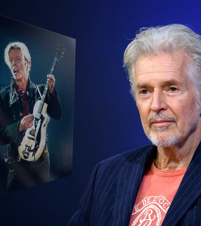 Ein älterer Mann mit grauem Haar und in T-Shirt und Jacket blickt mit einem dezenten Lächeln in die Kamera. Links von ihm ist ein Bild von einem Mann, der auf der Bühne E-Gitarre spielt, eingeblendet