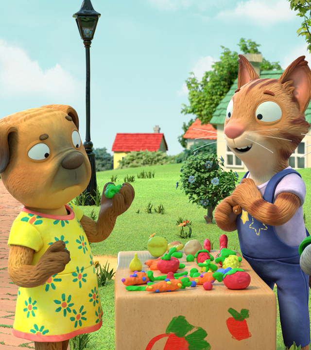 Frankie und Pip und Posy stehen an ihrem Stand, auf dem ihre gekneteten Gerichte liegen. Ein Mops steht auf der anderen Seite des Standes und sieht kritisch ein Stück Brokkoli an.