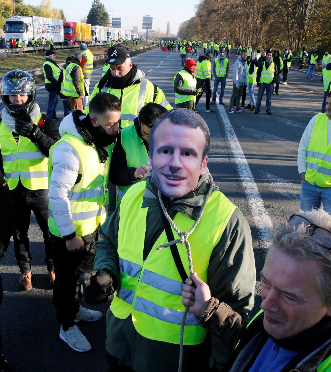 Demonstranten mit gelben Warnwesten laufen durch Frankreichs Straßen. Einer trägt eine Maske des französischen Präsidenten Macron am 17.11.2018 in Haulchin.