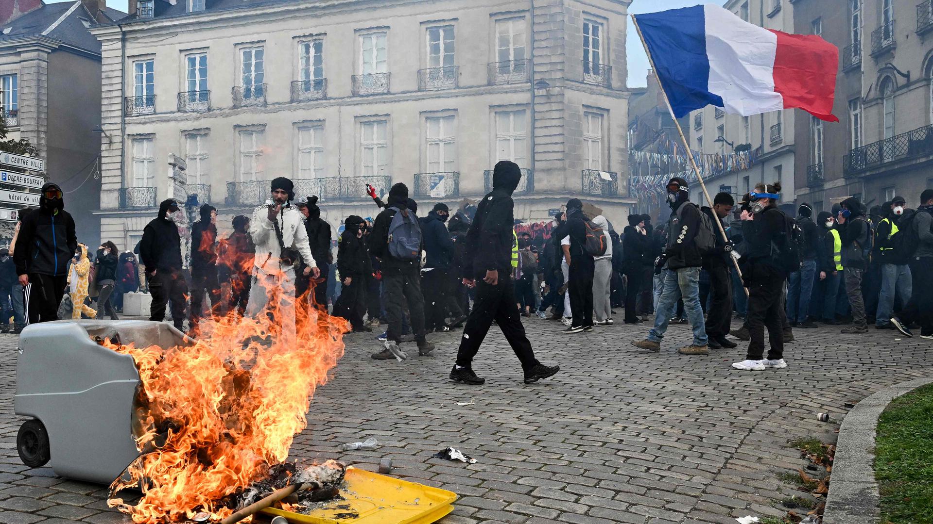Ein Demonstrant schwenkt eine französische Flagge neben einem brennenden Mülleimer während einer Demonstration.