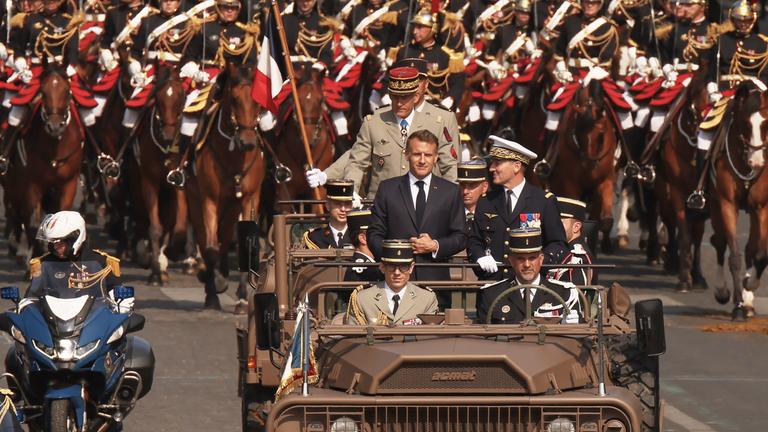 Der französische Präsident Macron steht zusammen mit dem Generalstabschef der französischen Streitkräfte, Mandon, im Kommandowagen während der Militärparade zum französischen Nationalfeiertag.