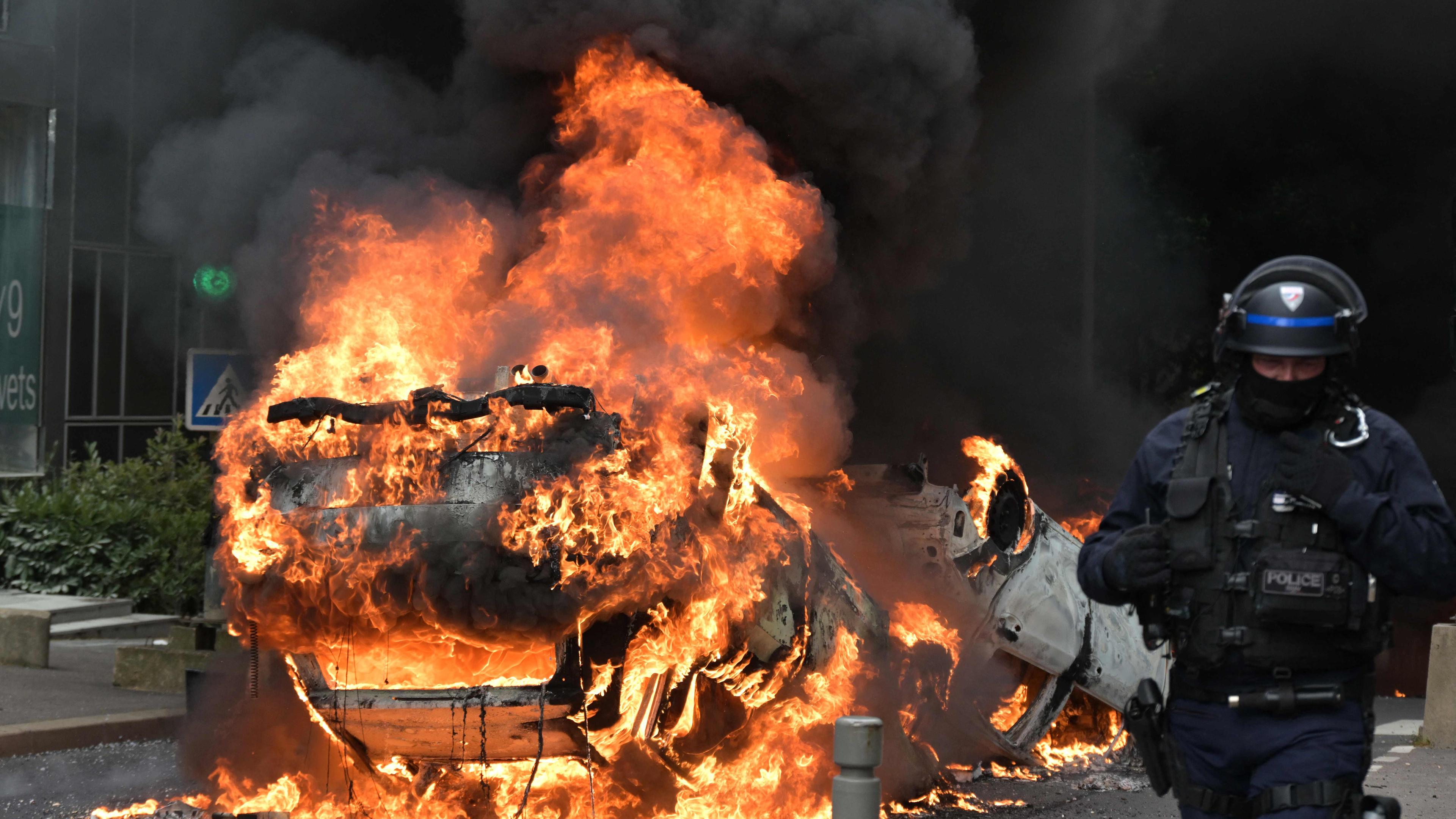 Ein Polizist steht neben einem brennenden Auto in Frankreich. 