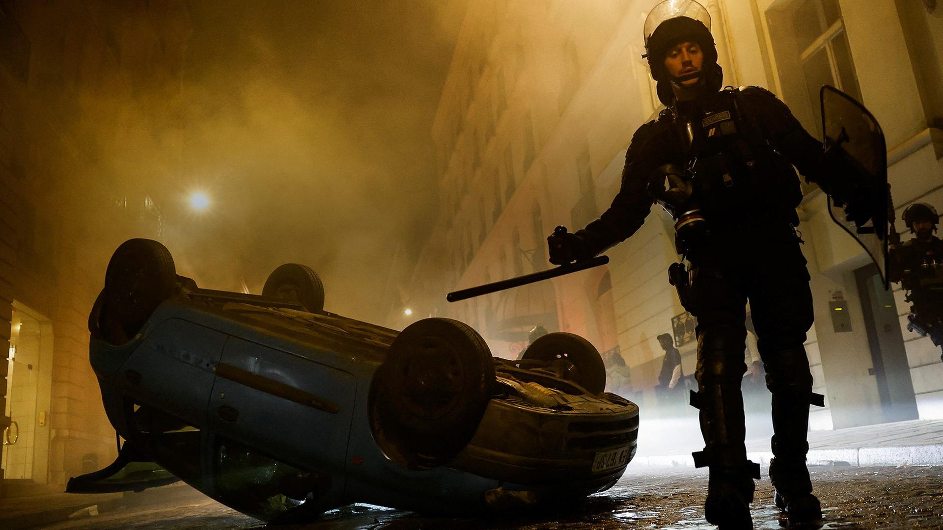 Ein Polizist steht nach gewaltsamen Protesten in Paris vor eine zersöten Auto. 