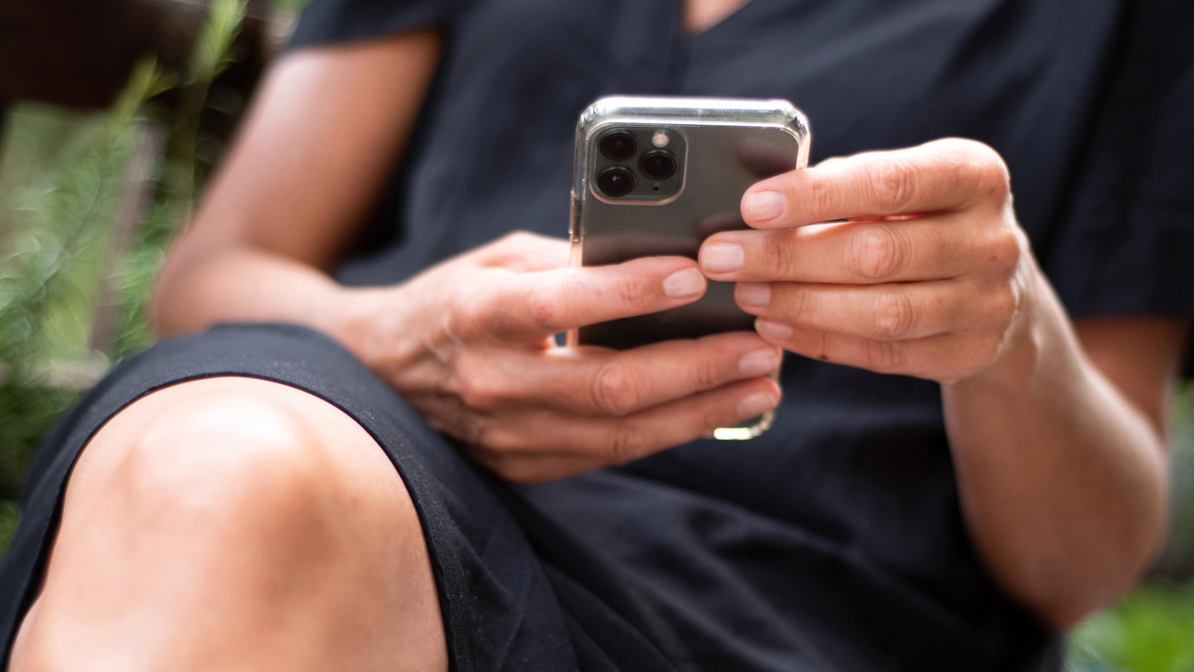 Eine Frau sitzt auf einer Bank und hält ein schwarzes Iphone in der Hand. 