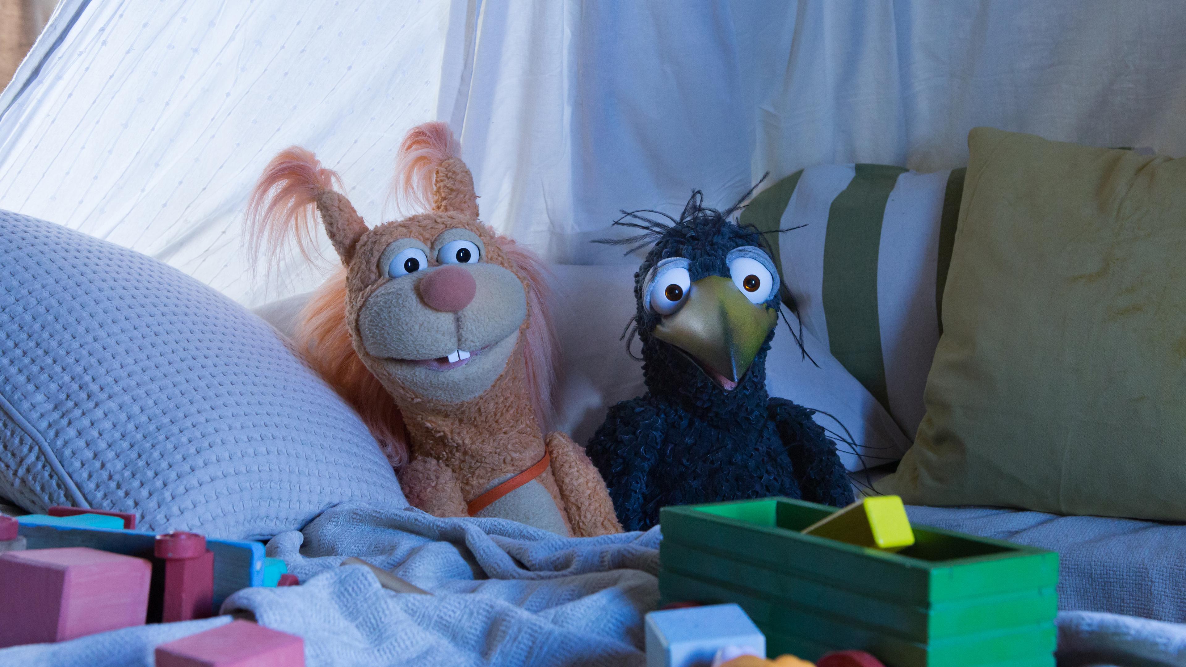 Ella und Rudi liegen bequem in der Kuschelecke und schauen gespannt ins Off auf einen Bildschirm, von dem das Licht auf sie fällt. Vor ihnen liegt verstreut Spielzeug.