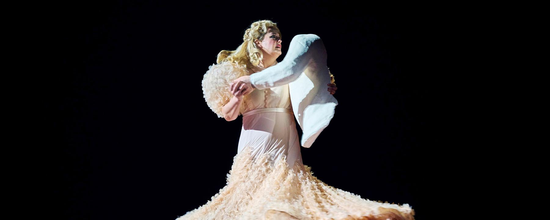 "Richard Strauss: Die Frau ohne Schatten": Tanzende Frau in einem champagnerfarbenen Abendkleid. Als Tanzpartner hält sie eine Puppe in Form eines Oberkörpers in den Armen.