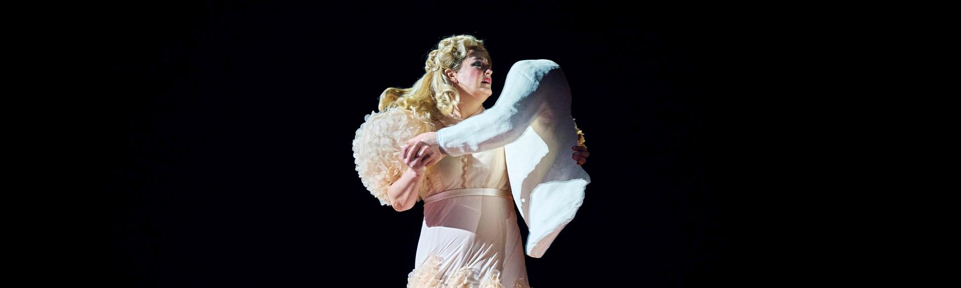 "Richard Strauss: Die Frau ohne Schatten": Tanzende Frau in einem champagnerfarbenen Abendkleid. Als Tanzpartner hält sie eine Puppe in Form eines Oberkörpers in den Armen.