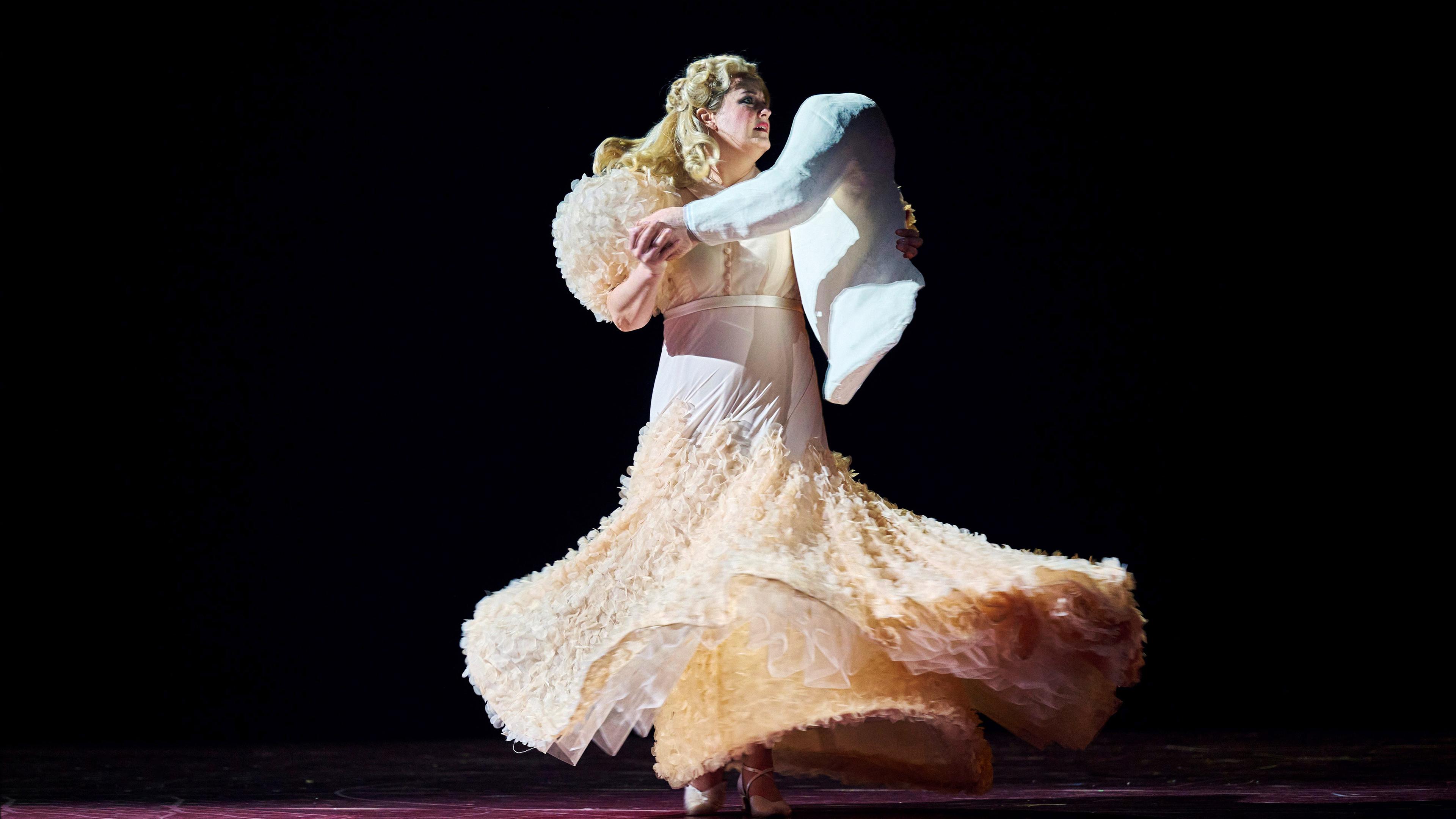 "Richard Strauss: Die Frau ohne Schatten": Tanzende Frau in einem champagnerfarbenen Abendkleid. Als Tanzpartner hält sie eine Puppe in Form eines Oberkörpers in den Armen.