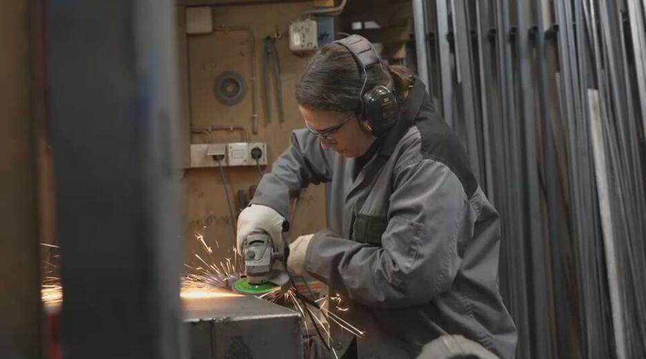 Die Ofenbauerin Laura Hack geht ihrer handwerklichen Tätigkeit nach. Sie trägt Schutzklamotten und eine Schutzbrille.