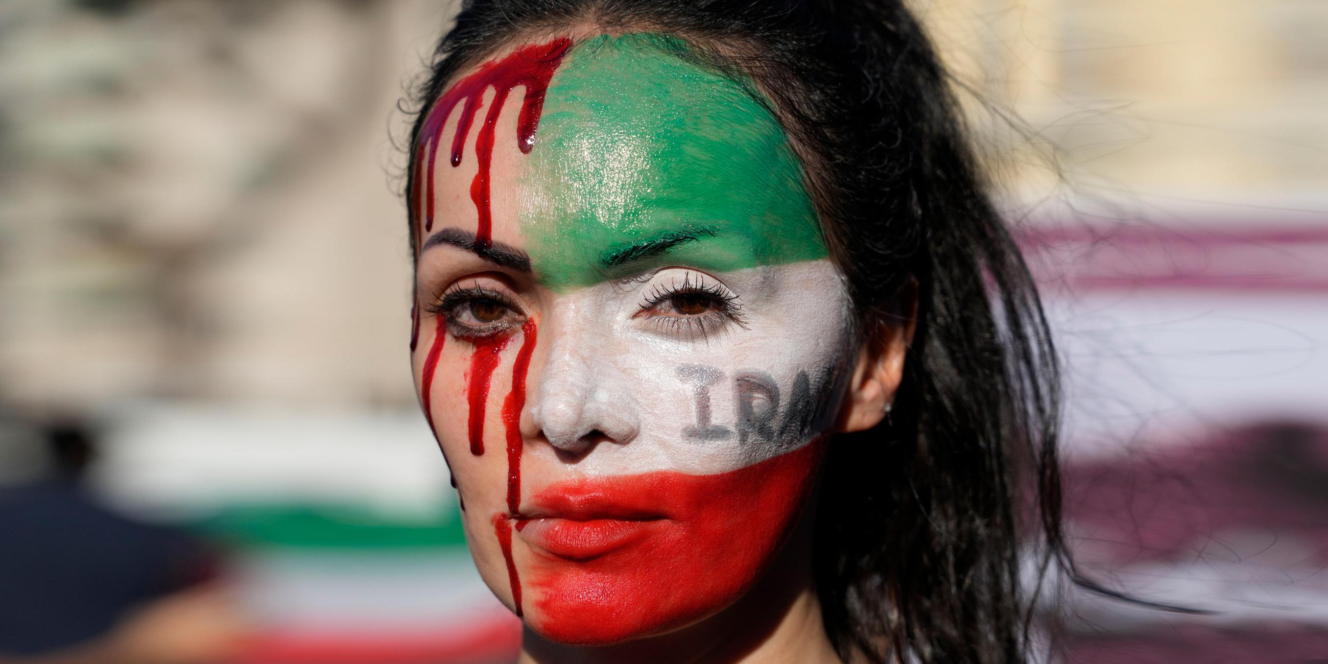 Eine Teilnehmerin einer Solidaritätsdemonstration mit den Protestierenden im Iran hat sich das Gesicht mit den Farben der iranischen Flagge und mit rotem Blut geschminkt.