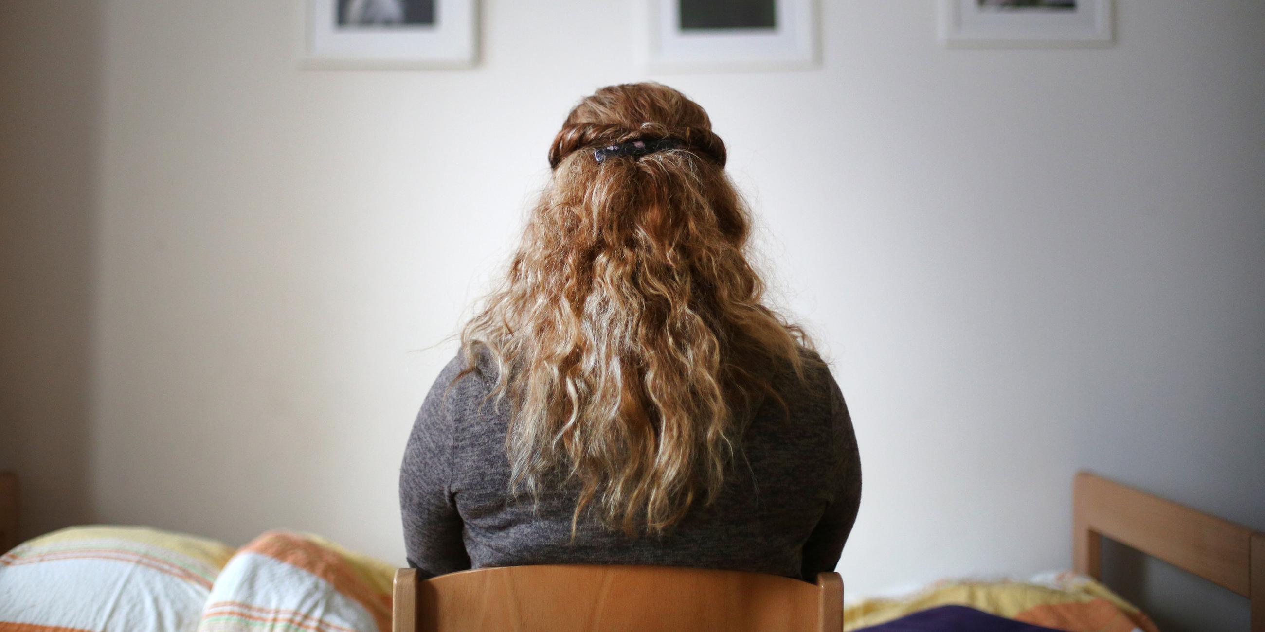 Eine Frau sitzt in einem Schlafzimmer eines Frauenhauses, zu sehen sind nur ihre blonden Locken von hinten; Oberhausen; 20.11.2016