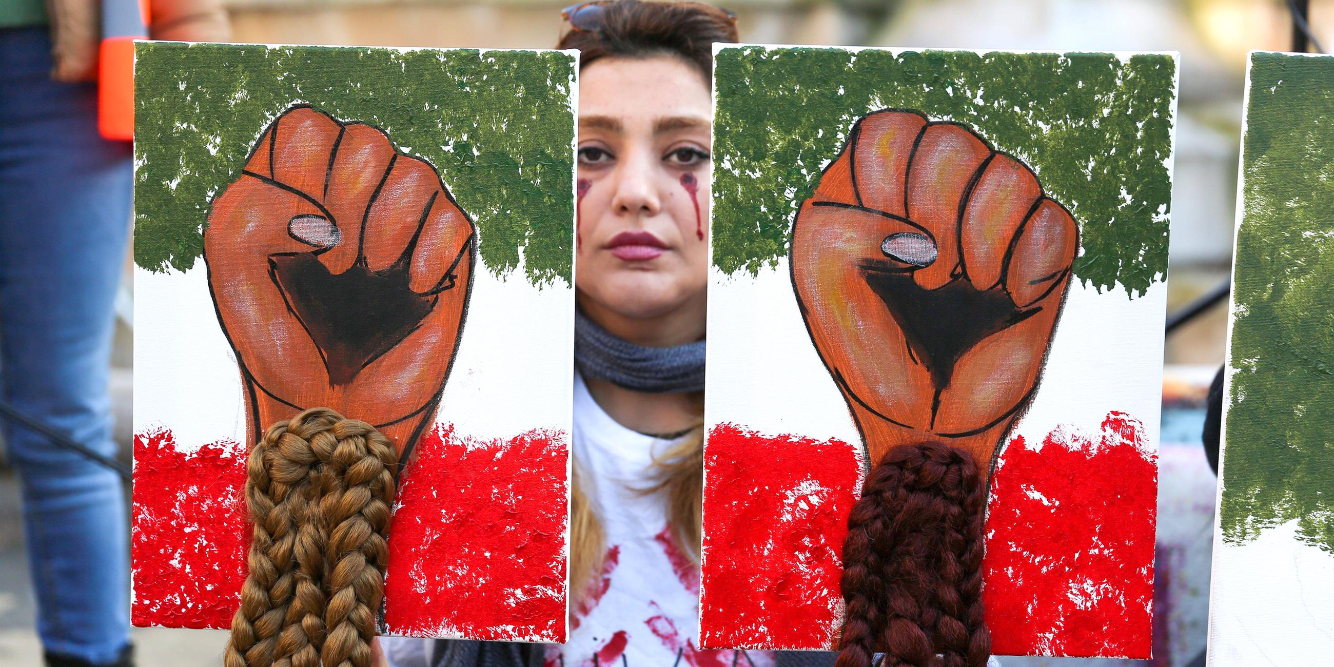 Auf einer Demonstration zur Unterstützung der iranischen Frauen in Paris hält eine Frau zwei Bilder hoch, auf die jeweils geballte Frauenfäuste und lange Zöpfe gemalt sind.