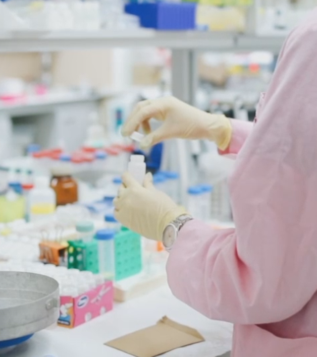 Frau in Labor mit Schutzanzug schraubt Reagenzglas auf. Sie trägt Einmalhandschuhe. Links daneben: Lichtschematische Darstellung eines Fingerabdrucks.