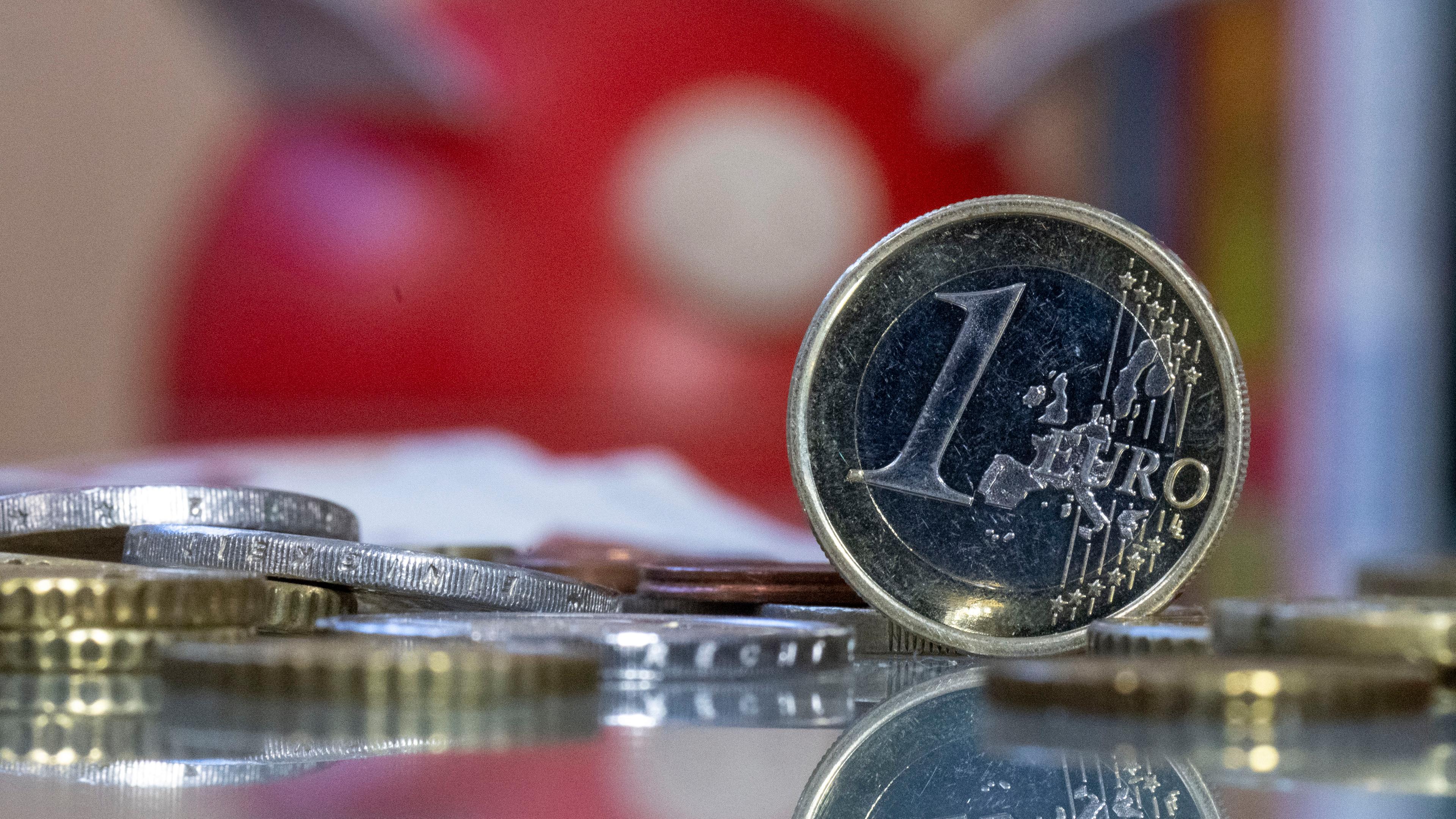 Ein 1 Euro-Stück steht neben mehreren Geldstücken, welche über den Tisch verstreut liegen.