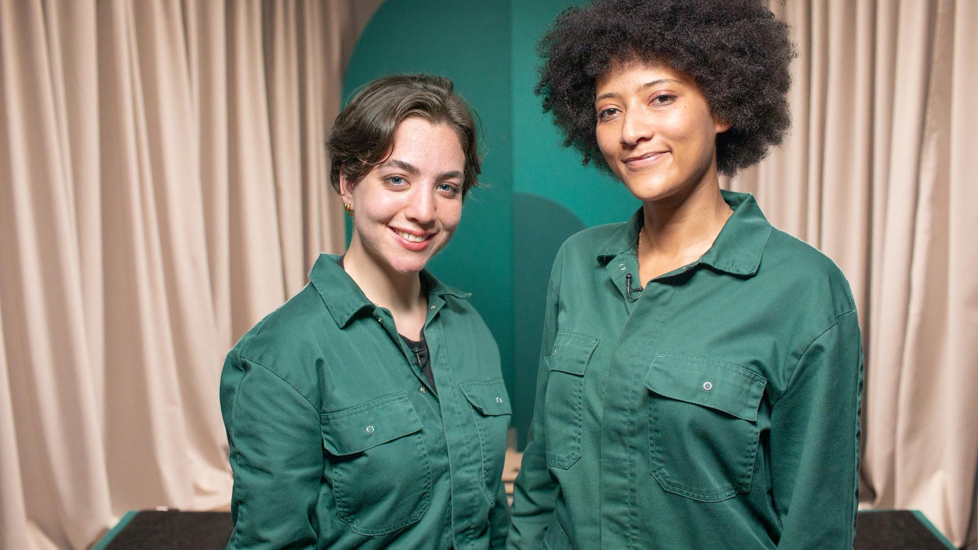 Zwei Frauen in grünen Overalls blicken in die Kamera
