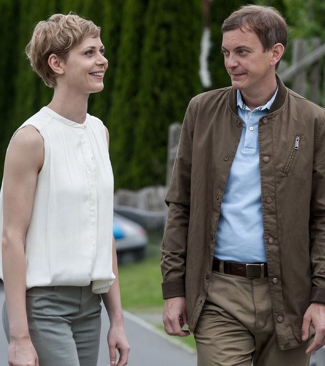 "Der Bergdoktor - Fremdes Herz (2)": Hanna Hofer (Katharina Schlothauer) und Michael Lanzinger (Daniel Krauss) stehen auf der Wiese einer Sommerrodelbahn. Er sieht sie an, sie lacht.