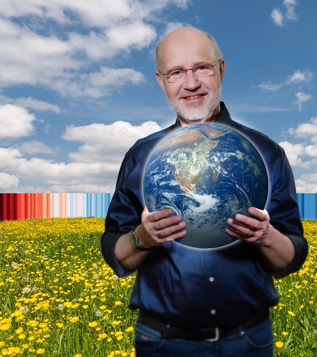 Harald Lesch auf Wiese mit Globus in der Hand.