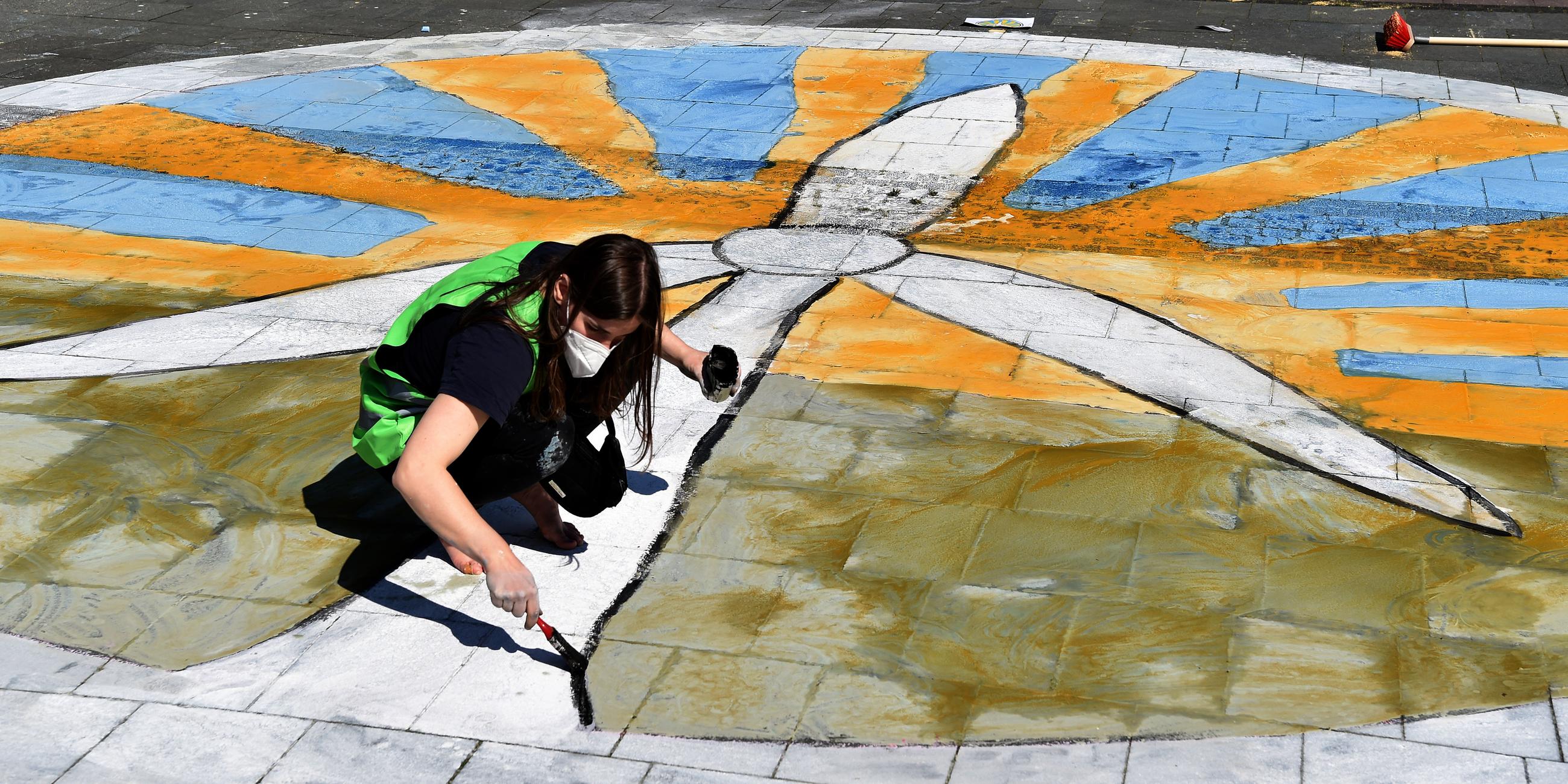 Eine Fridays for Future-Aktivistin malt ein Windkraftrad vor Sonne auf den Boden