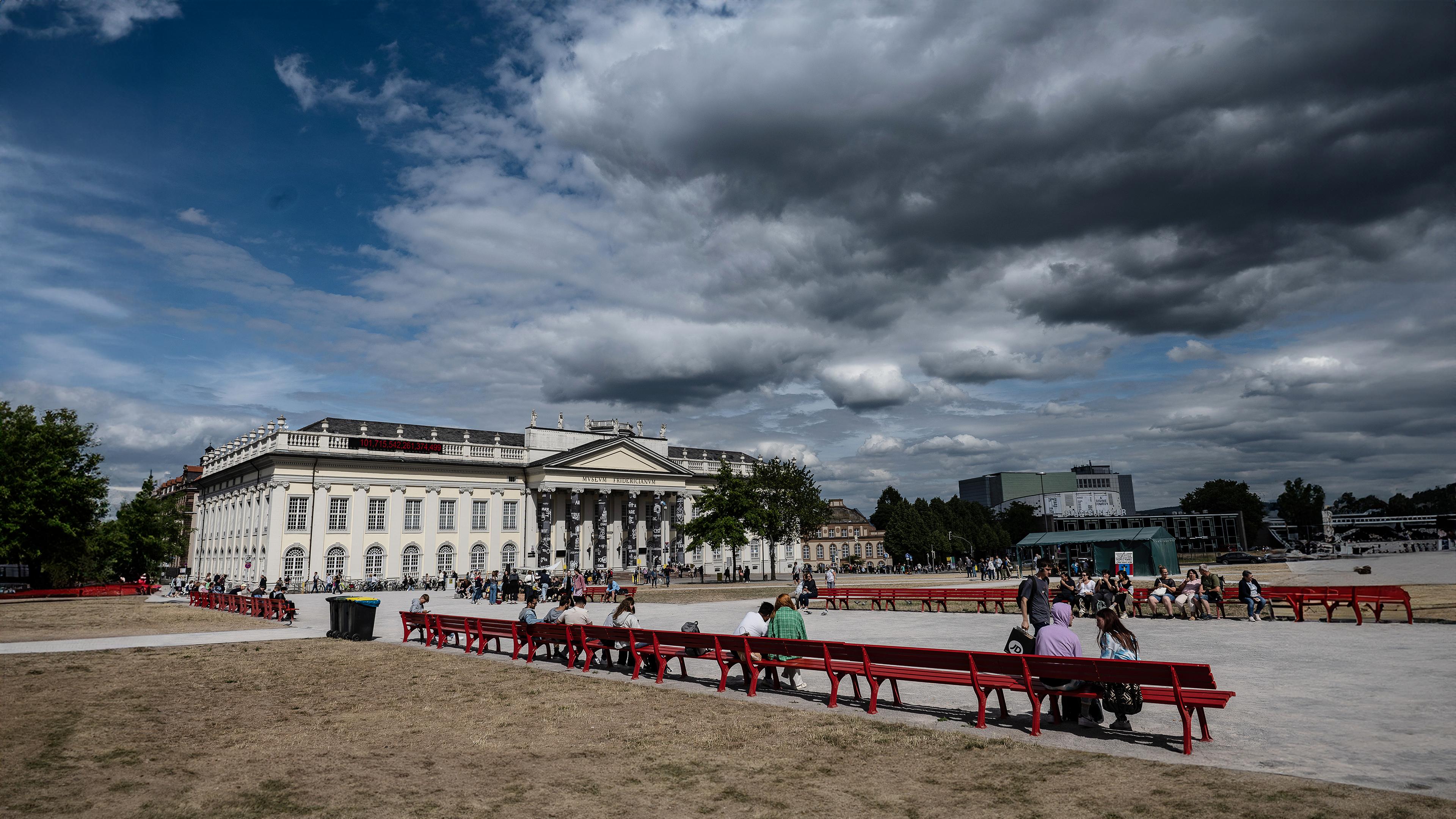 Über dem historischen Gebäude des Museum Fridericianum in Kassel ballen sich dunkle Wolken. Im Park davor sind Spaziergänger unterwegs.