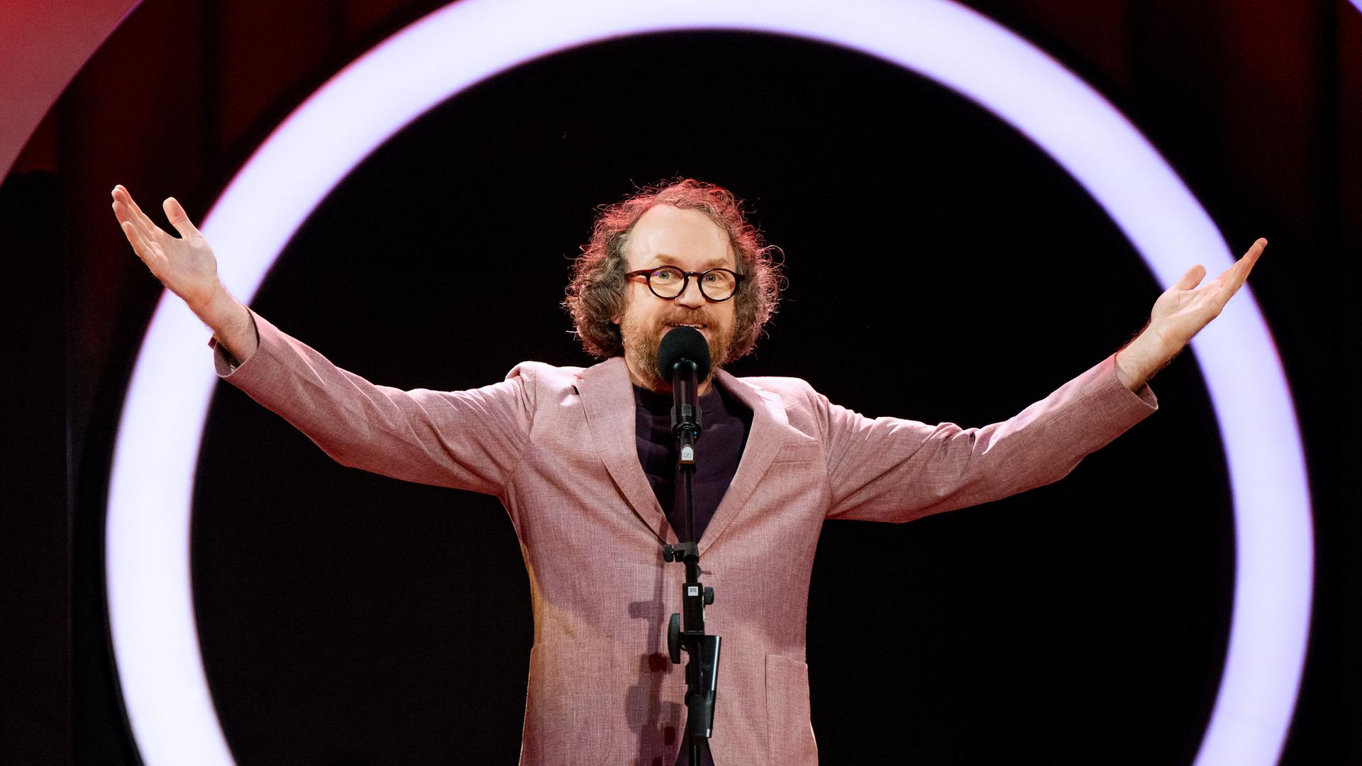 Friedemann Weise steht auf der Bühne und streckt seine Arme zur Seite aus.