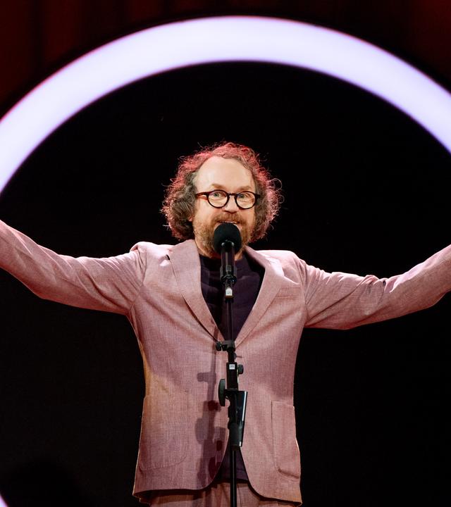 Friedemann Weise steht auf der Bühne und streckt seine Arme zur Seite aus.