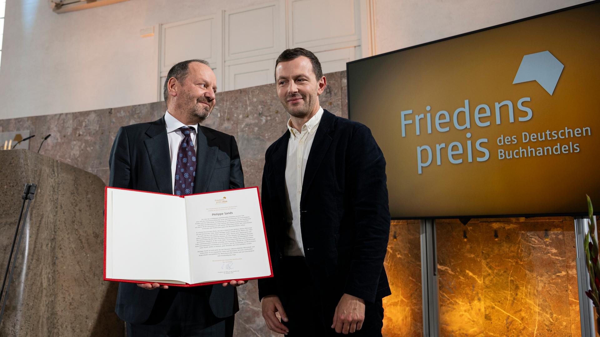 Philippe Sands, und Sebastian Guggolz, Vorsteher des Börsenvereins des Deutschen Buchhandels, stehen während der Preisverleihung auf der Bühne.