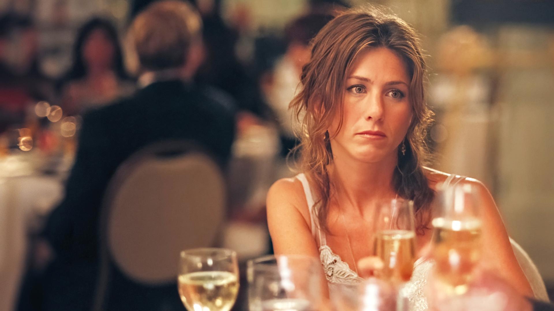 "Friends With Money": Olivia (Jennifer Aniston) sitzt an einem Tisch voller Gläser und schaut frustriert ins Leere.