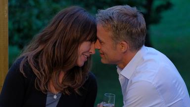 "Frühling - Das verlorene Mädchen": Katja (Simone Thomalla) und Mark (Marco Girnth) sitzen unter einem Sonnenschirm im Garten und haben die Köpfe aneinander gelegt. Sie lächeln. Mark hat ein Sektglas in der Hand.