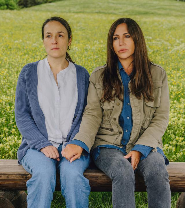 Katja Baumann (Simone Thomalla) sitzt mit Maria Ronzheimer (Judith Toth) auf einer Bank auf einer Wiese und hält ihre Hand.