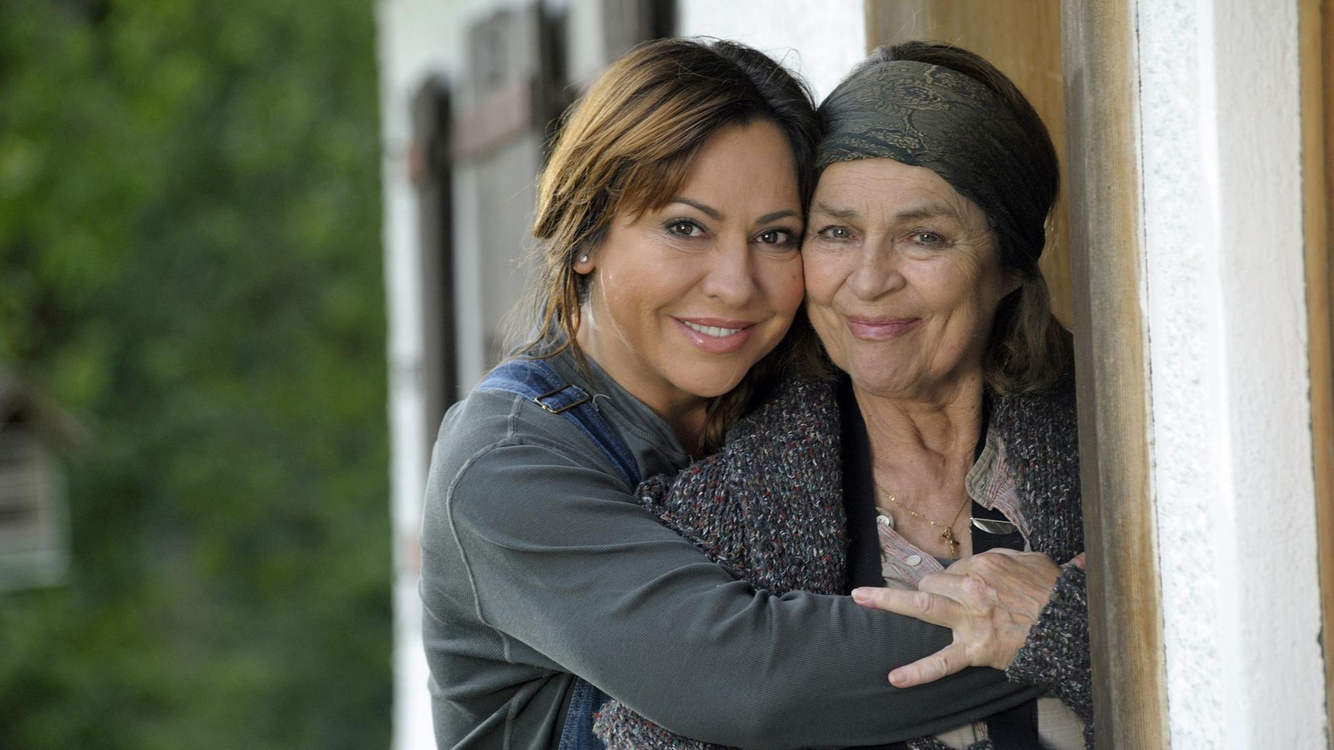 "Frühling zu zweit": Die Dorfhelferin Katja Baumann (Simone Thomalla) umarmt die Bäuerin Maria Sindlfinger (Cornelia Froboess) - beide schauen nach vorne. Im Hintergrund: Hauswand und Sträucher