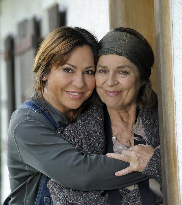 "Frühling zu zweit": Die Dorfhelferin Katja Baumann (Simone Thomalla) umarmt die Bäuerin Maria Sindlfinger (Cornelia Froboess) - beide schauen nach vorne. Im Hintergrund: Hauswand und Sträucher