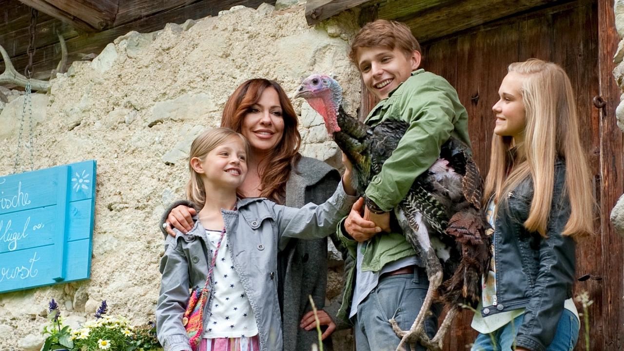 Katja mit den drei Kindern auf dem elternlosen Hof der Familie Böhm. Der Sohn hält einen Truthahn im Arm, der von allen beobachtet wird (von links: Flora Li Thiemann, Simone Thomalla, Merlin Rose, Nadine Kösters).