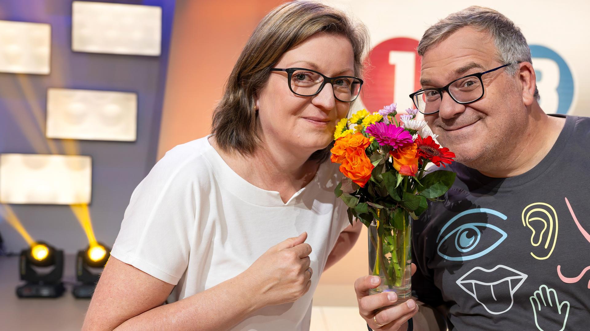"1, 2 oder 3 - Fühlen, riechen, staunen": Prof. Dr. Jessica Freiherr steht mit Elton hinter einem Pult im Studio. Sie hält eine Duftprobe in einem kleinen Glasbehälter in der Hand. Im Hintergrund ist das "1, 2 oder 3"- Logo zu sehen.