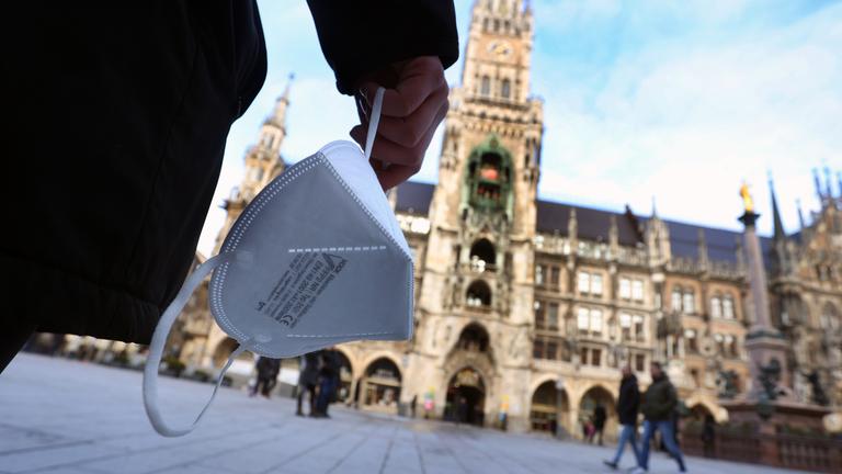 Typical für die Corona-Krise: Eine Hand hält eine FFP2-Maske, im Hintergrund das Münchner Rathaus