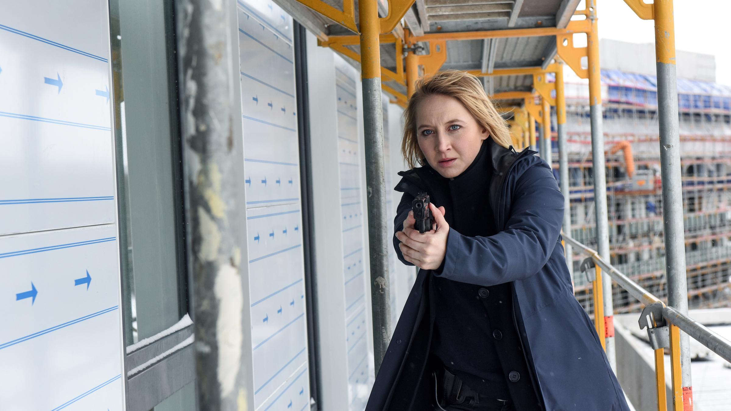 Nora (Anna Maria Mühe) steht mit gezogener Waffe auf einem Baugerüst einer Baustelle.