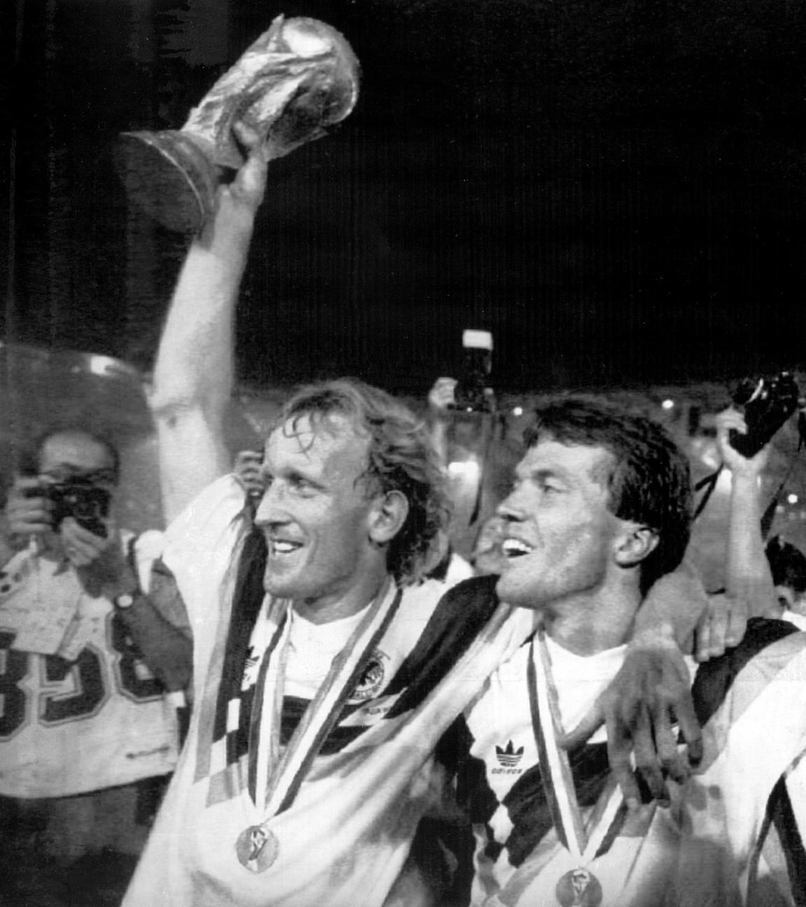 08.07.1990, Italien, Rom: Die damaligen deutschen Nationalspieler Andreas Brehme (l-r), mit dem WM-Pokal in der Hand, Lothar Matthäus und Pierre Littbarski bejubeln den Erfolg im Olympiastadion in Rom.