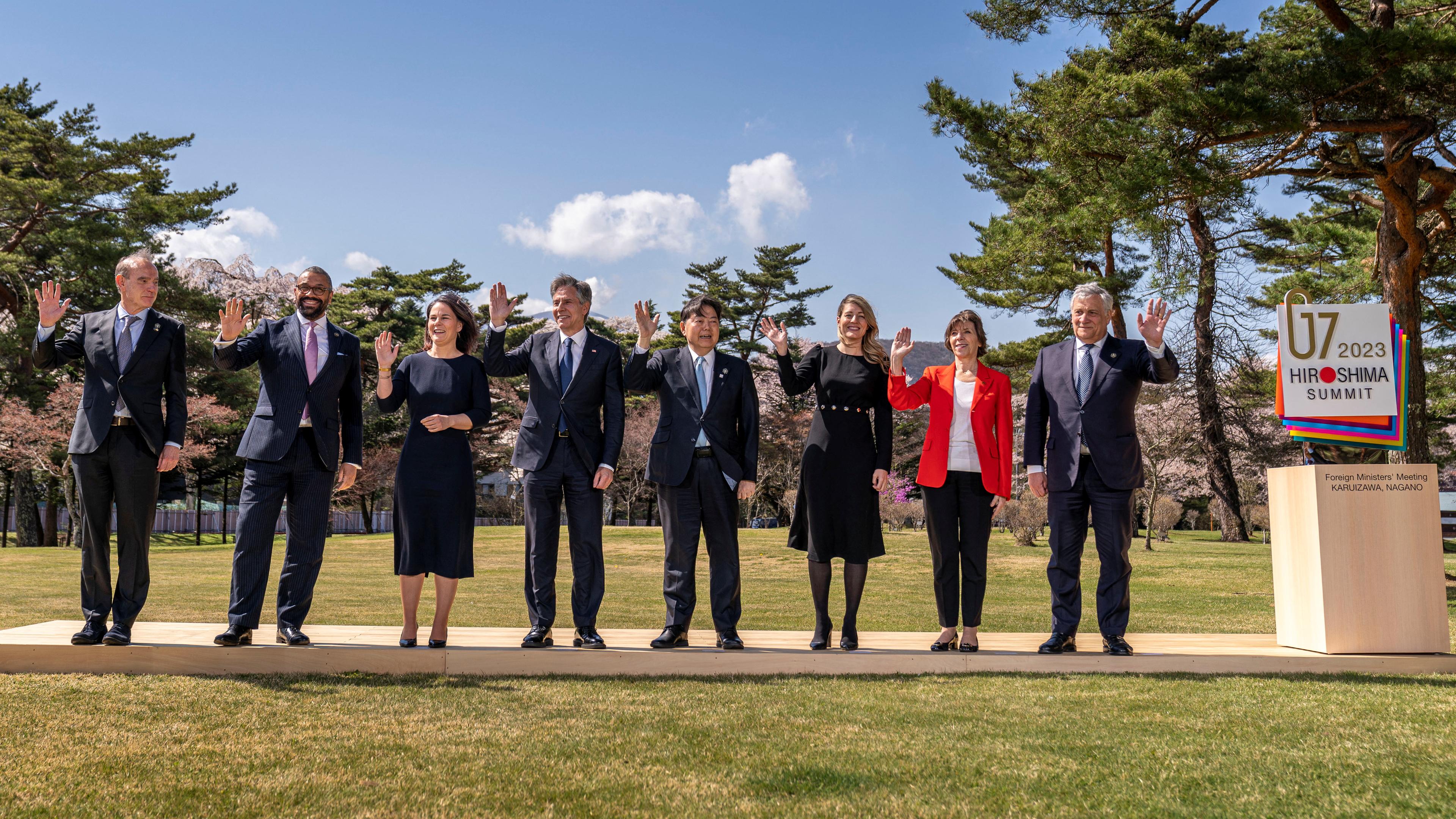 Die Außenministerinnen und Außenminister der G7 staaten stehen nebeninander auf einer Wiese und winken in die Kamera.