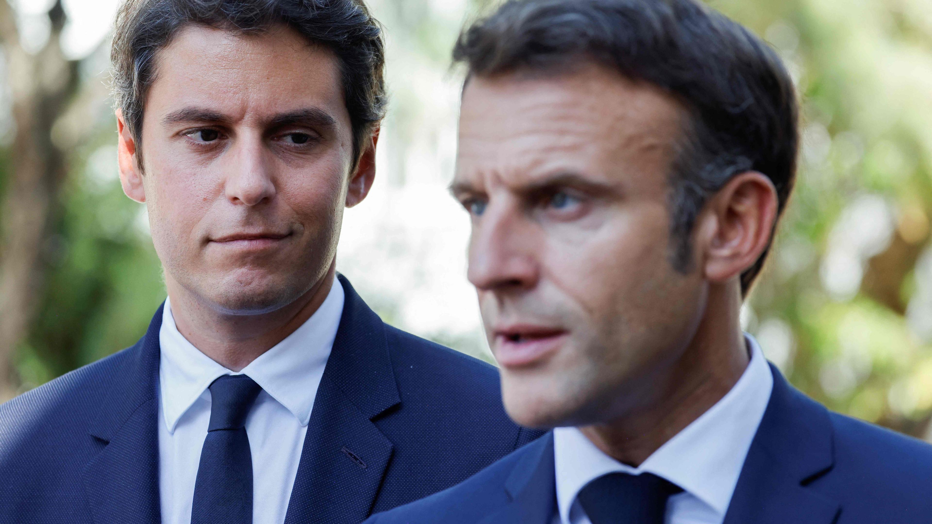 Der französische Bildungs- und Jugendminister Gabriel Attal (l.) blickt auf die Rede des französischen Präsidenten Emmanuel Macron (r.)
