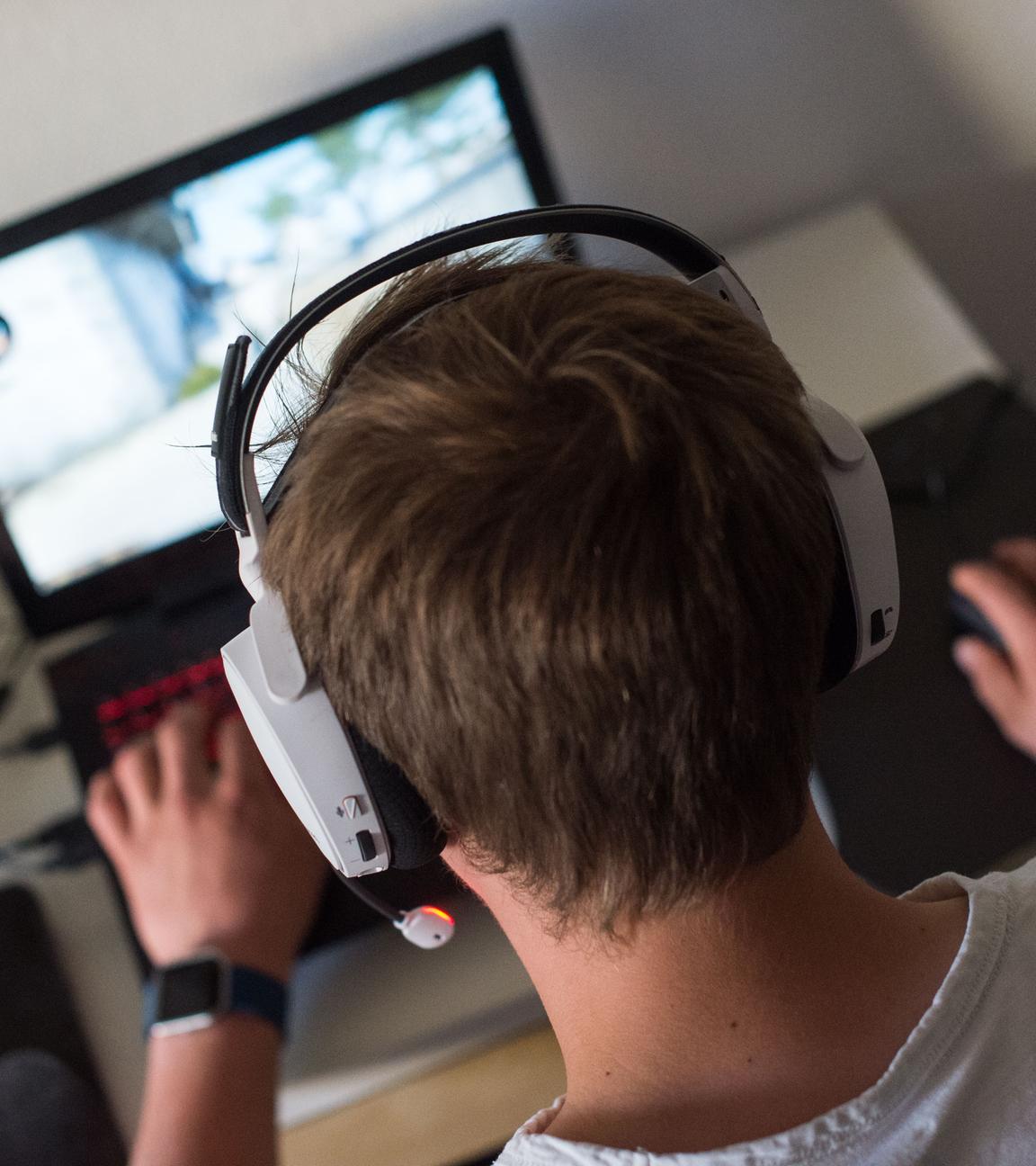 Ein Jugendlicher sitzt mit einem Headset vor einem Laptop und spielt ein Online-Computerspiel.