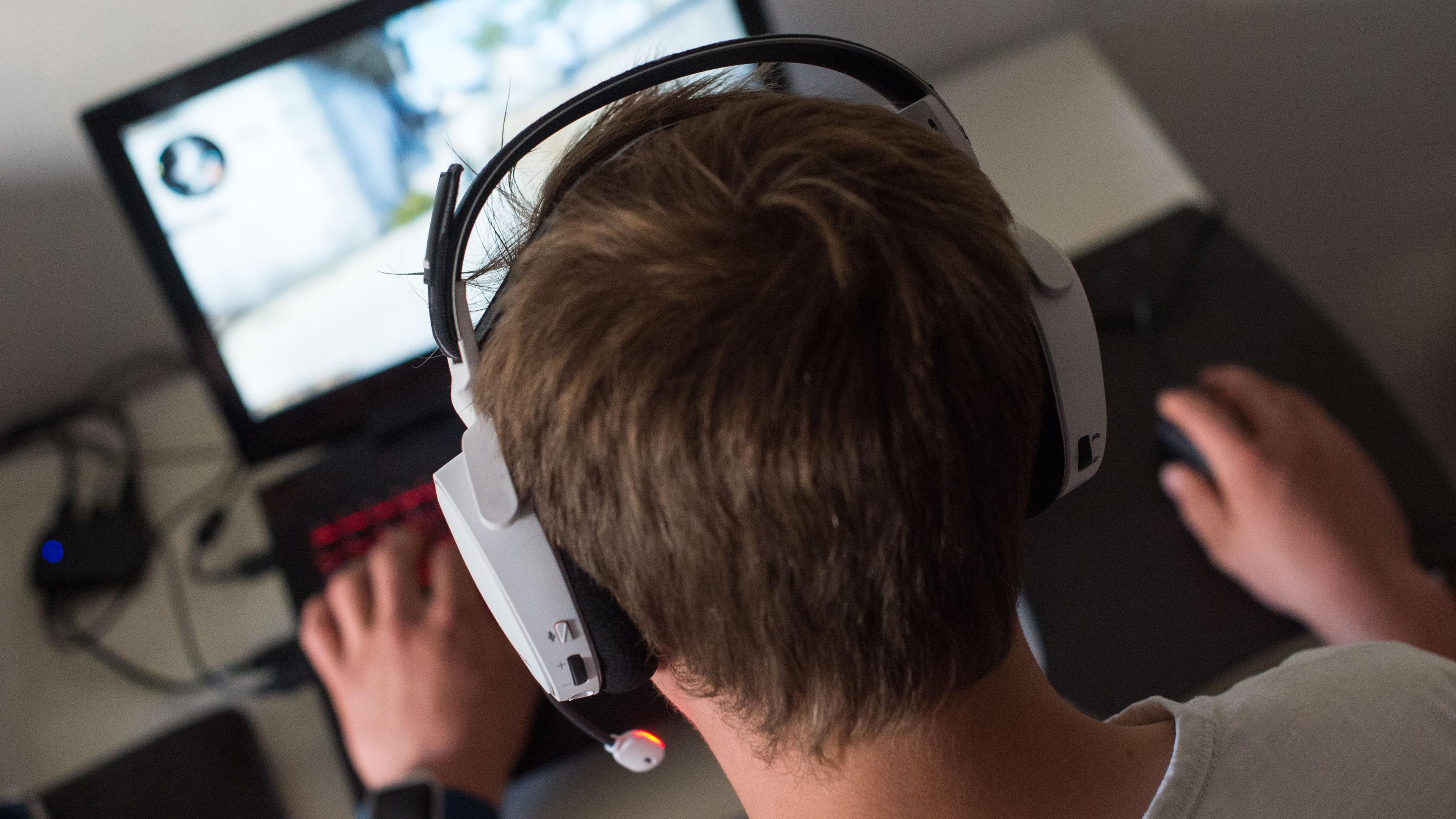 Ein Jugendlicher sitzt mit einem Headset vor einem Laptop und spielt ein Online-Computerspiel.