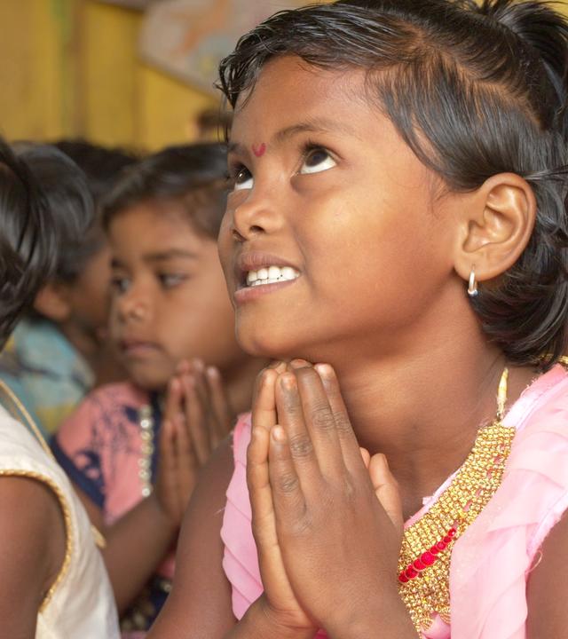  Eine Gruppe Mädchen, die Augen nach oben gerichtet, die Hände aneinander gelegt.