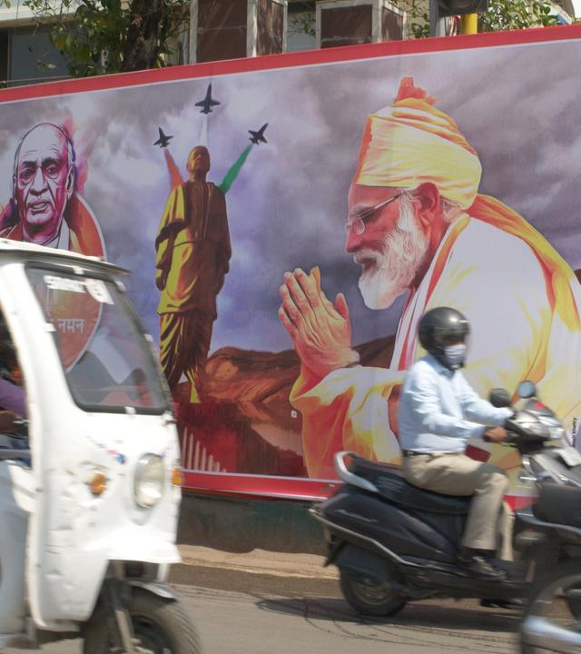  Straßenszene mit Mopeds, großes Wahlplakat der Regierungspartei BJP, auf dem Premierminister Narendra Modi zu sehen ist.