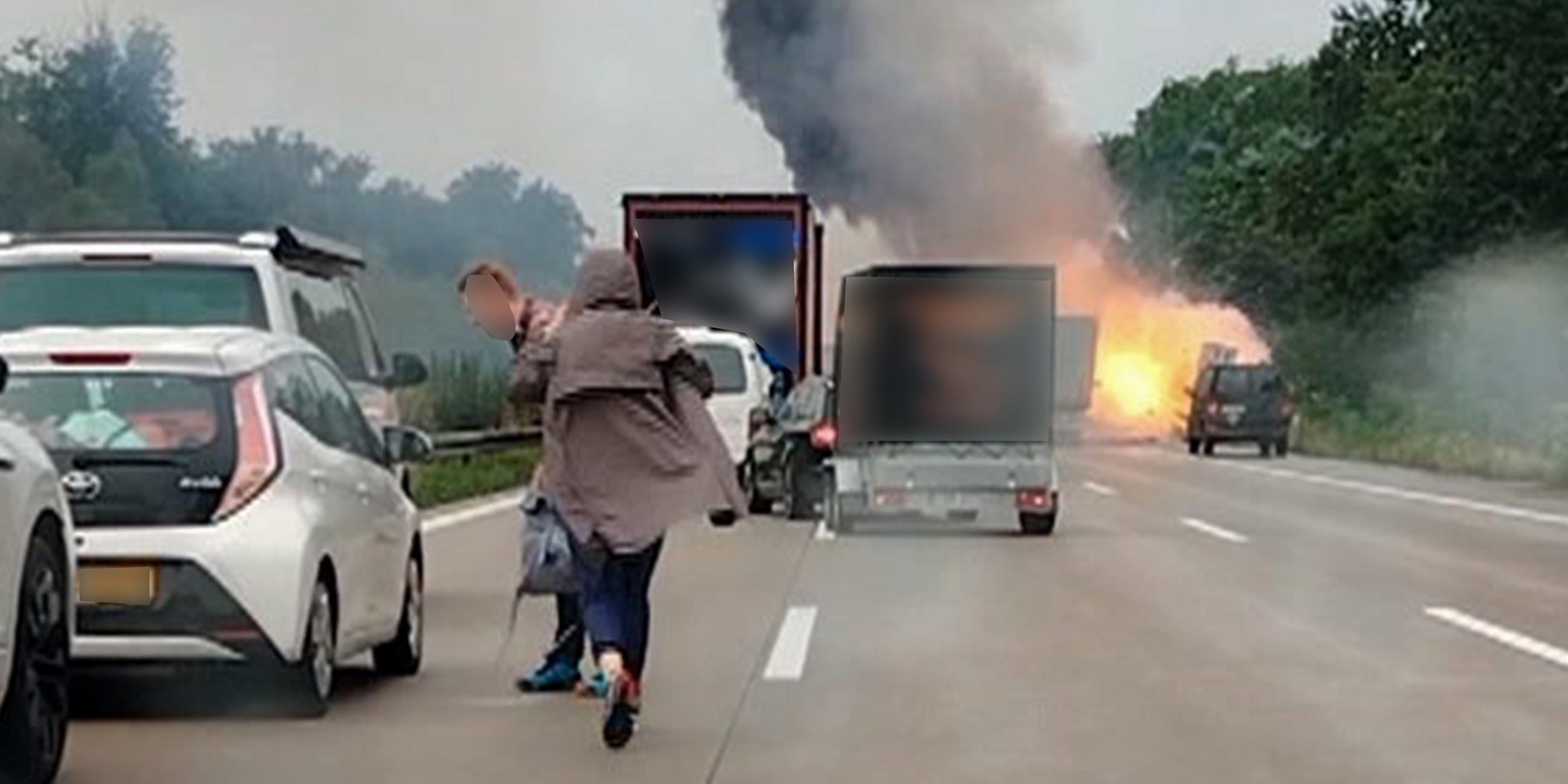 Autofahrer verlassen ihre Fahrzeuge, während im Hintergrund ein LKW in Flammen steht.