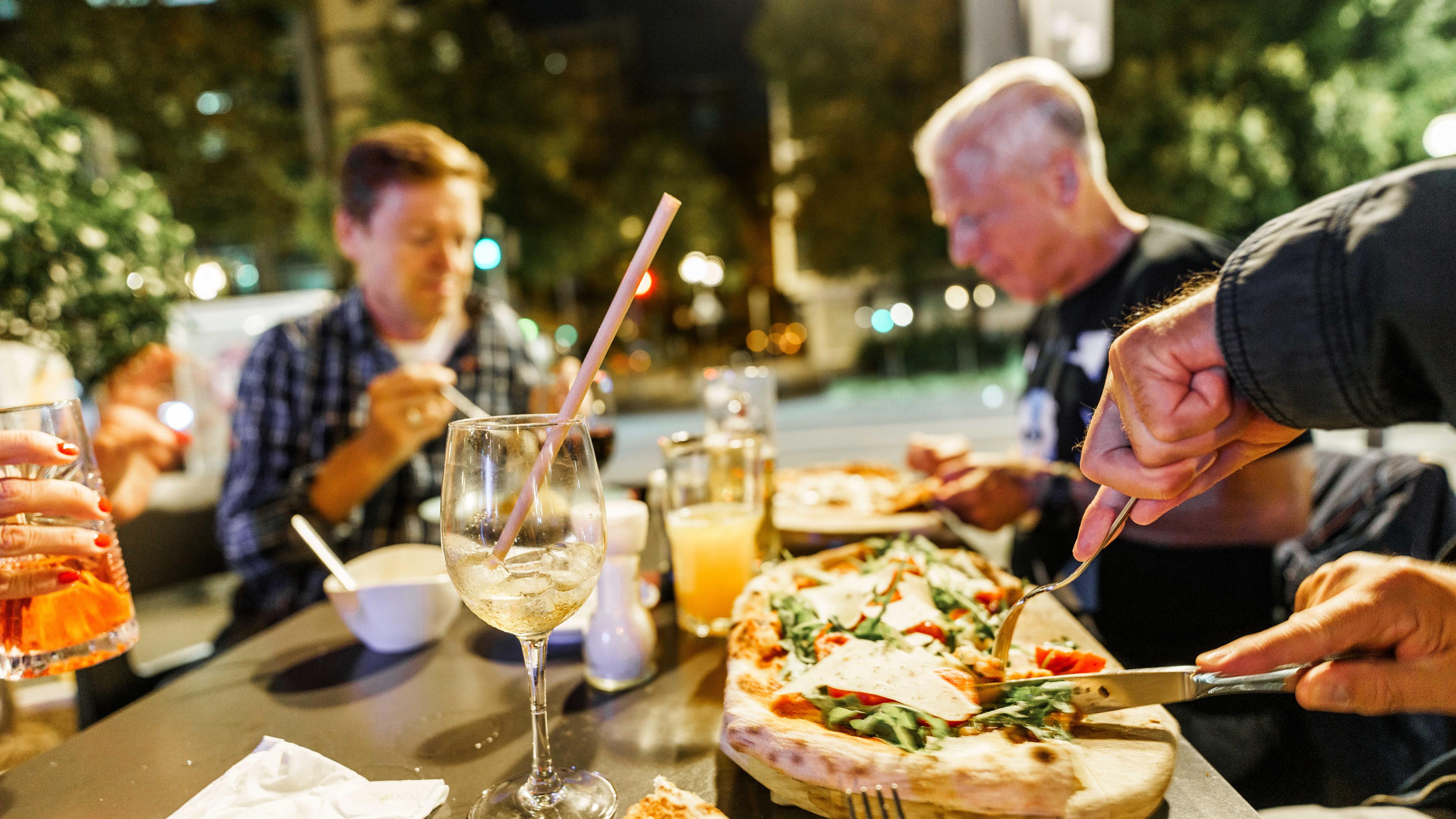 Menschen sitzen im Außenbereich eines Restaurants und essen u.a. Pizza.
