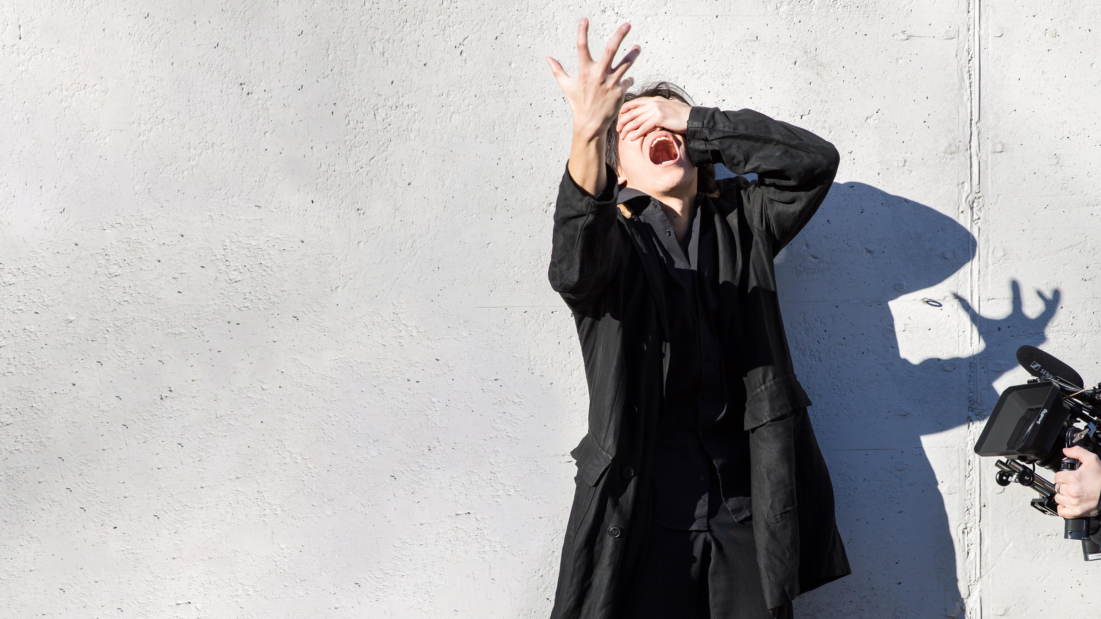 Choreografin und Tänzer haben die Arme verschränkt vor dem Gesicht. Eine Hand auf der Stirn, eine zur Seite. Sie blicken nach links.