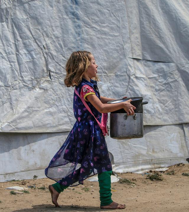 Ein intern vertriebenes palästinensisches Mädchen trägt Töpfe zu ihrer Familienunterkunft, nachdem sie Essen aus einer Wohltätigkeitsküche in Jabalia im nördlichen Gazastreifen erhalten hat.