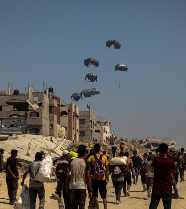 Menschen in Gaza warten am Boden auf herabfallende Fallschirme mit Lebensmittelpaketen. 
