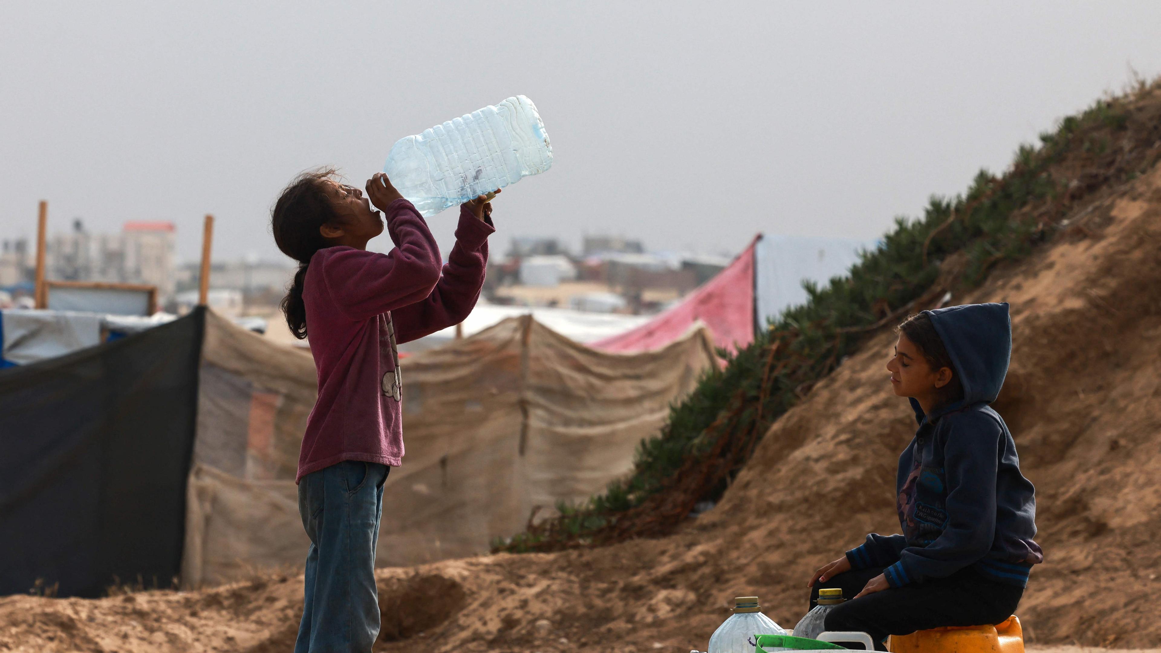 Zwei palästinensische Kinder warten in einem Flüchtlingscamp in Rafah darauf, ihre Wasserbehälter aufzufüllen.