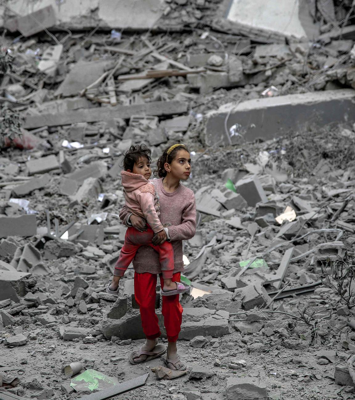 Gaza-Stadt: Ein palästinensisches Mädchen steht inmitten von Trümmern und hält ein kleineres Kind auf dem Arm. 